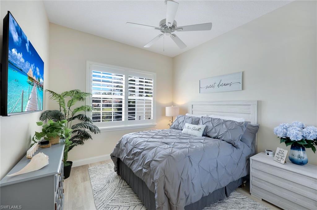 3108 Dominica Way Naples, FL 34119 - Photo 15 of 39 Bedroom featuring wood-finish flooring, vaulted ceilings, a ceiling fan, and plantation shutters onlooking the pool with a lake view.