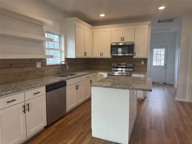 a living room with stainless steel appliances kitchen island hardwood floor and a large window