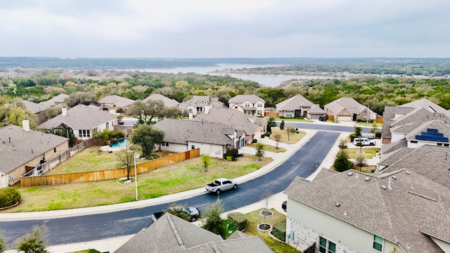 117 Rock Dock Road Georgetown, TX 78633 - Photo 39 of 39 An aerial view of the property and its surrounding neighborhood, featuring a curving street, manicured lawns, and mature trees, with a body of water visible in the distance