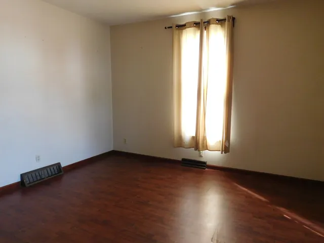 an empty room with wooden floor and windows with curtains