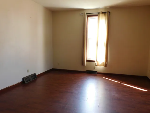 an empty room with wooden floor and windows with curtains