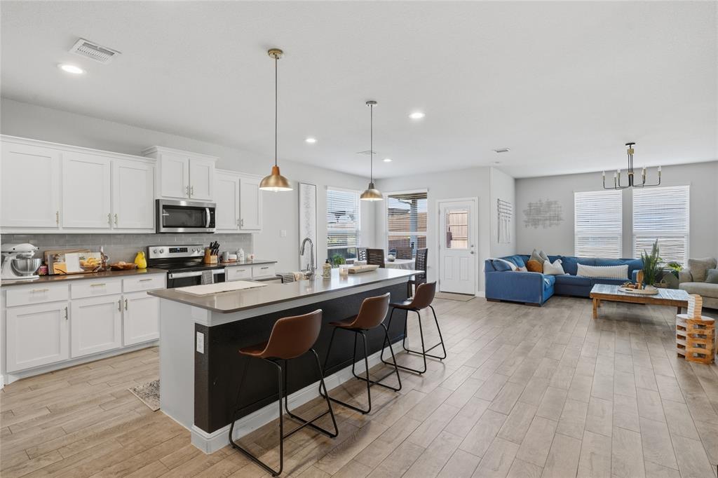 1812 Ruffian Road Granbury, TX 76049 - Photo 11 of 37 Open-concept living area featuring a kitchen island with pendant lighting, white cabinetry, integrated stainless steel appliances, and wood-finish flooring throughout