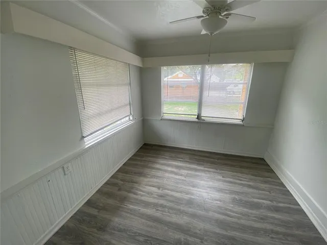 an empty room with wooden floor fan and windows