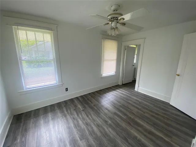 an empty room with wooden floor fan and windows