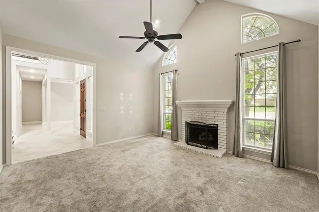a view of a livingroom with a fireplace a ceiling fan and windows