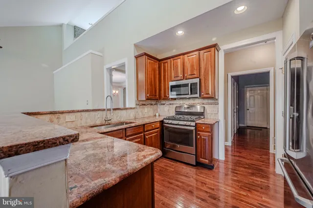 a kitchen with stainless steel appliances granite countertop a sink a stove and a wooden cabinets