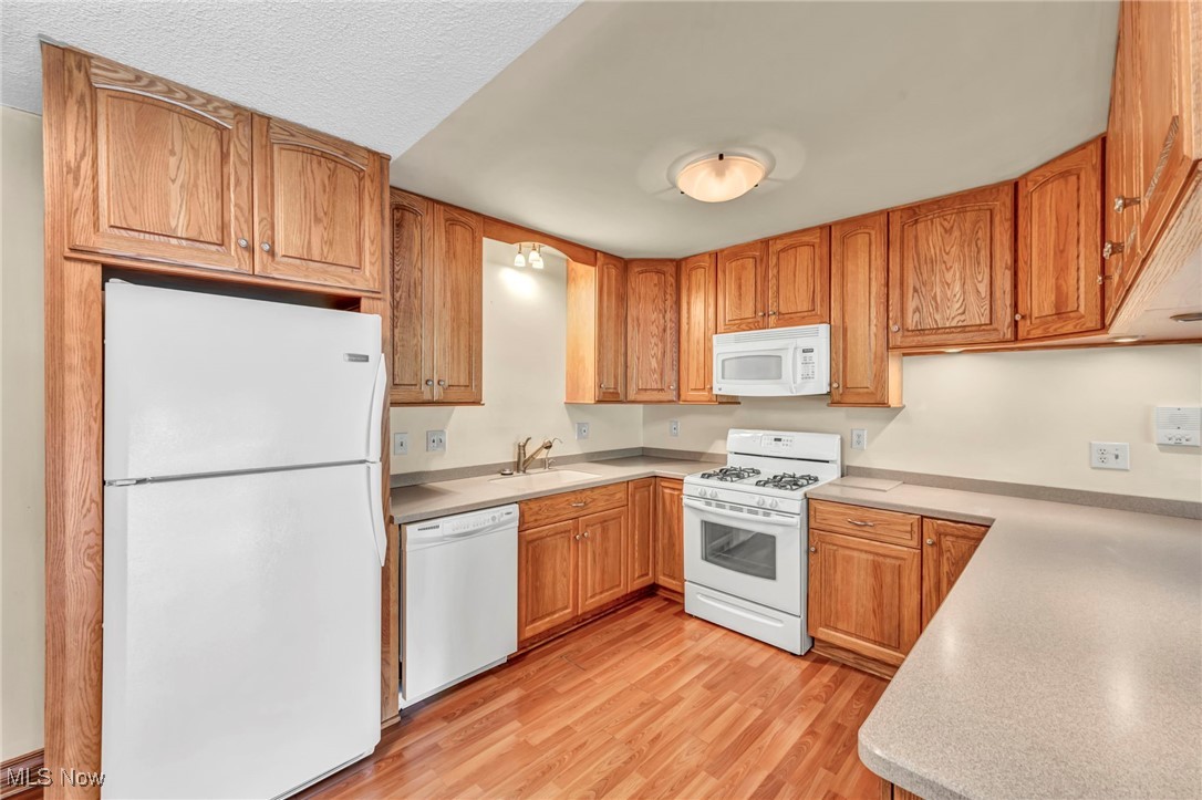 1263 Lost Nation Road, Unit 5 Willoughby, OH 44094 - Photo 13 of 26 Kitchen featuring white appliances, light wood-style floors, light countertops, brown cabinets, and a textured ceiling