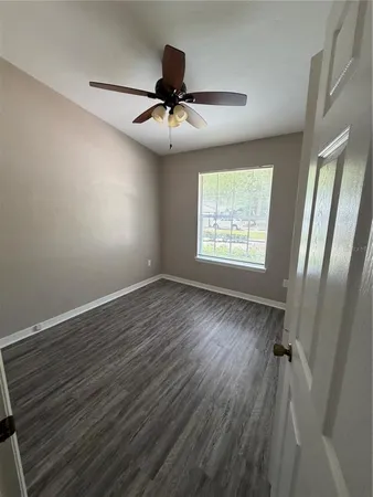 an empty room with wooden floor fan and windows