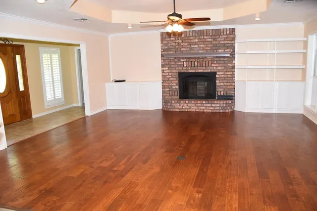 an empty room with wooden floor fireplace and windows