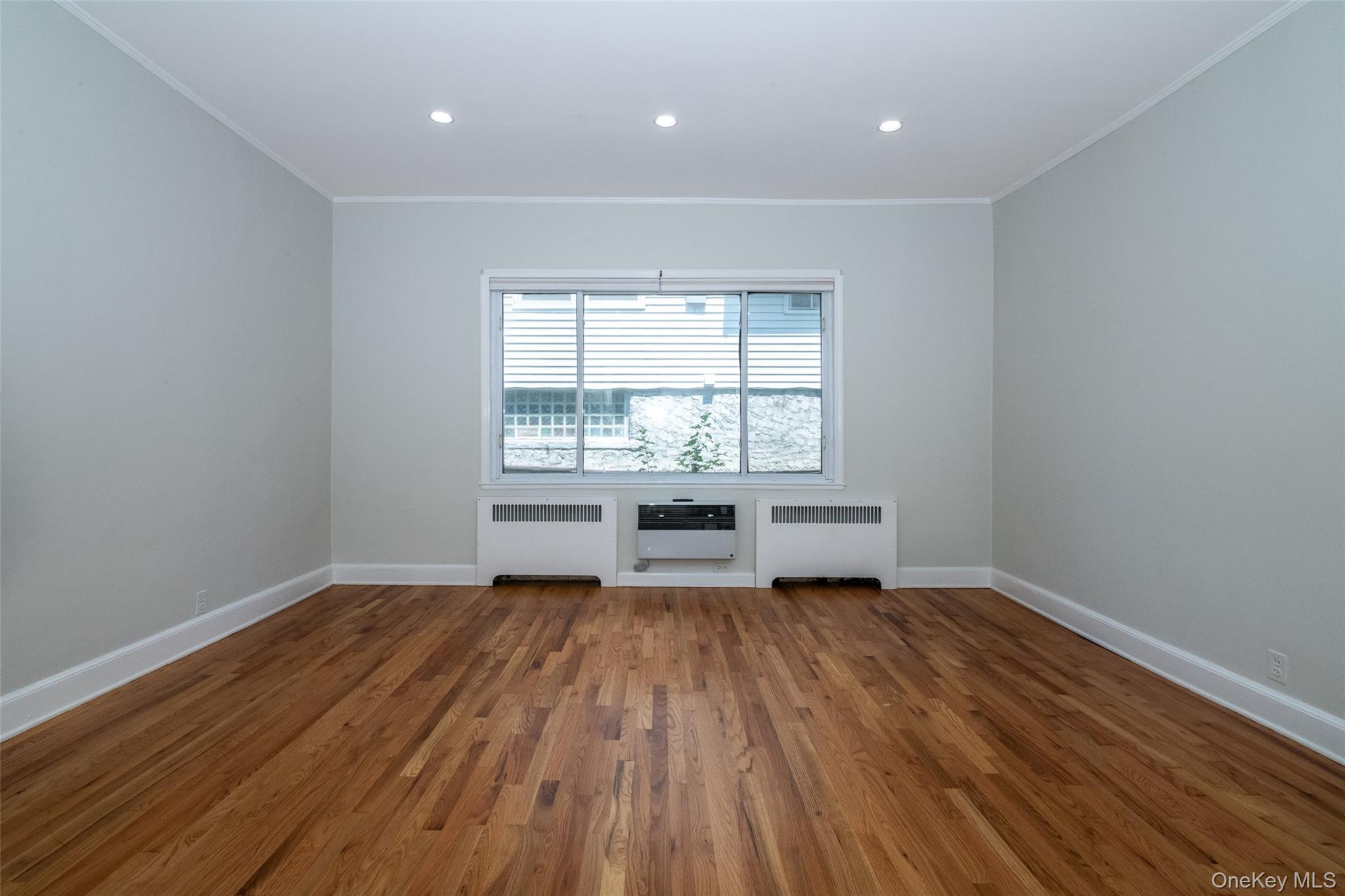 7 Alpha Place, Unit FIRST New Rochelle, NY 10805 - Photo 15 of 25 Empty room with radiator, crown molding, wood finished floors, a wall mounted air conditioner, and recessed lighting