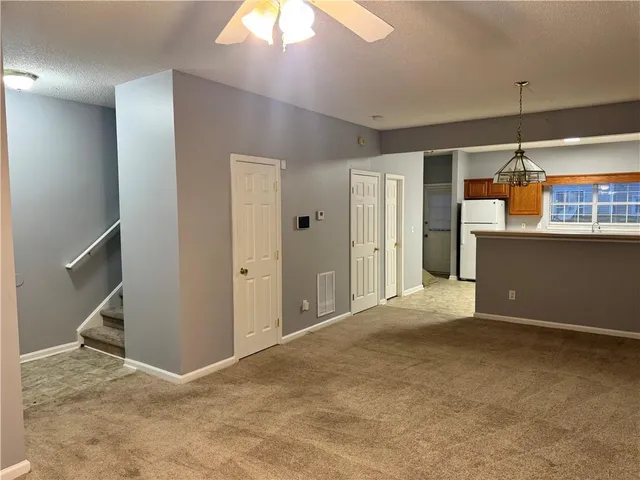 an empty room with kitchen view and a chandelier fan