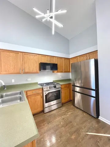 a kitchen with stainless steel appliances granite countertop a refrigerator a sink dishwasher a stove and white countertops with wooden floor