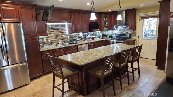 a kitchen with stainless steel appliances granite countertop a dining table chairs refrigerator and a sink