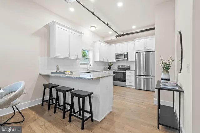 a kitchen with stainless steel appliances granite countertop a refrigerator a stove a sink a dining table and chairs with wooden floor