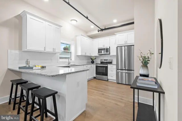 a kitchen with granite countertop a refrigerator oven a sink dishwasher and white cabinets with wooden floor