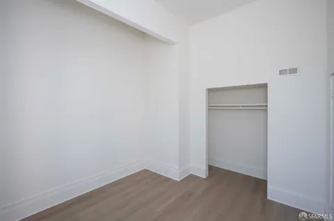 a view of an empty room with closet and wooden floor