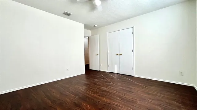 an empty room with wooden floor chandelier fan and windows