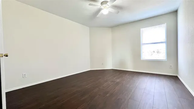 an empty room with wooden floor ceiling fan and windows