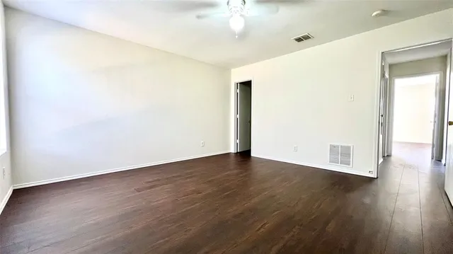 an empty room with wooden floor fan and windows