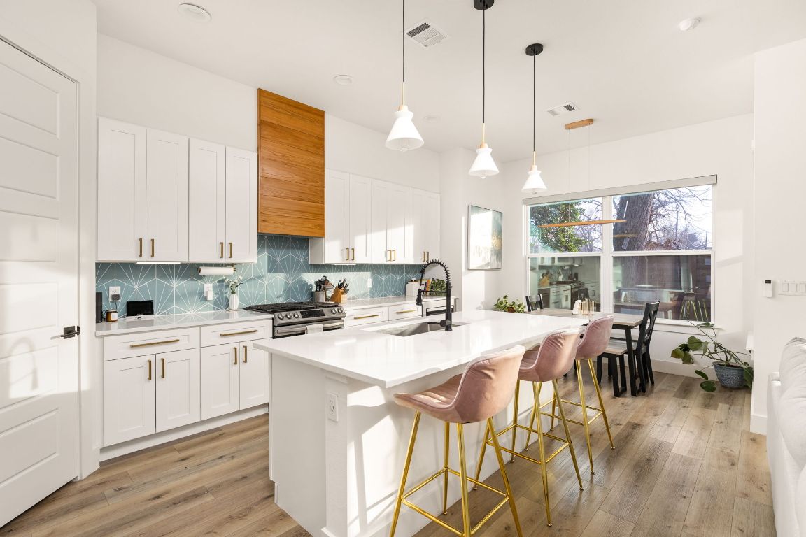 5109 Glissman Road, Unit 1 Austin, TX 78702 - Photo 5 of 39 Kitchen with white cabinets, hanging light fixtures, a center island with sink, decorative backsplash, and light wood-type flooring