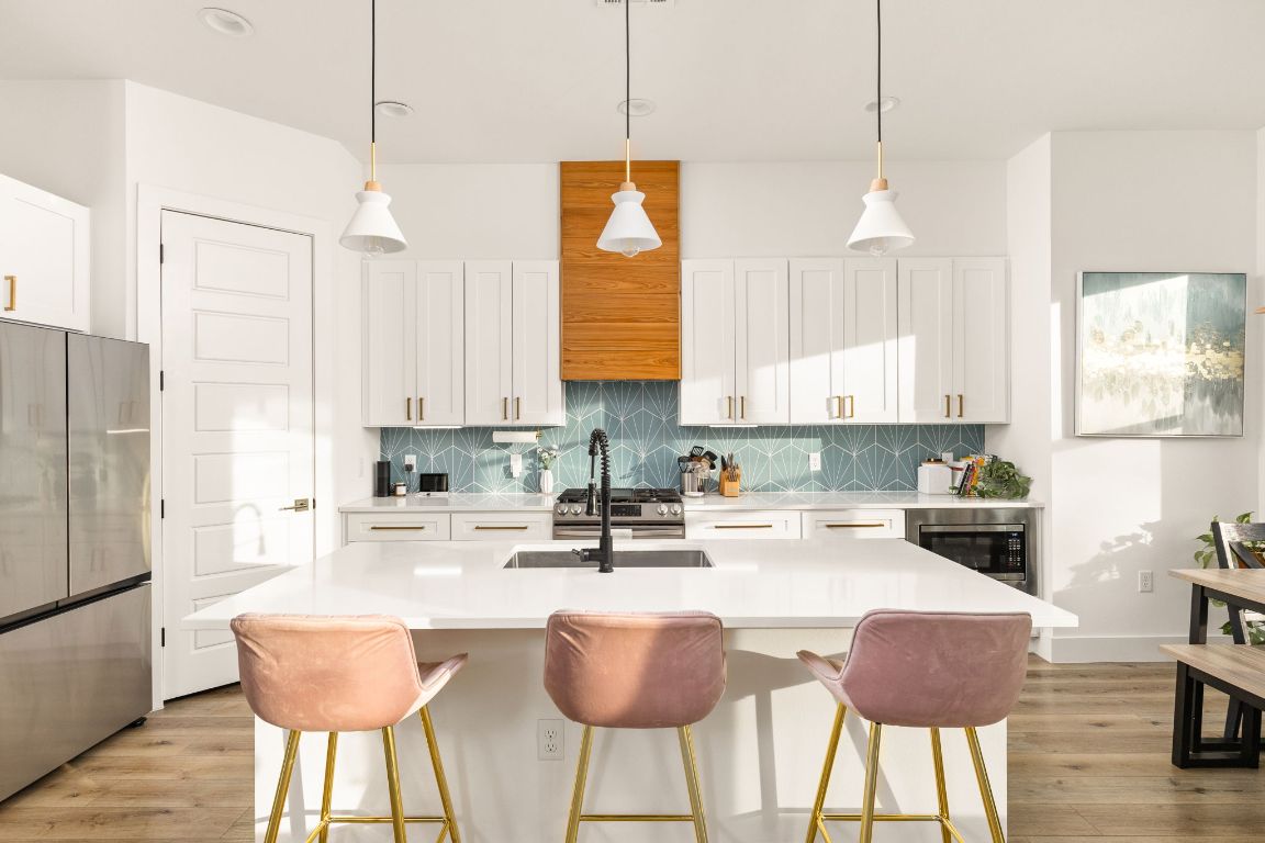 5109 Glissman Road, Unit 1 Austin, TX 78702 - Photo 6 of 39 Kitchen with hanging light fixtures, stainless steel appliances, white cabinetry, light wood-style floors, and an island with sink