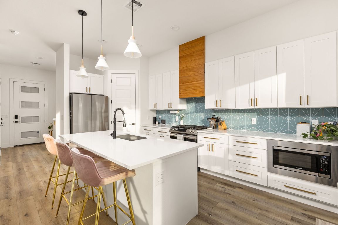 5109 Glissman Road, Unit 1 Austin, TX 78702 - Photo 7 of 39 Kitchen featuring white cabinetry, hanging light fixtures, a center island with sink, appliances with stainless steel finishes, and a breakfast bar