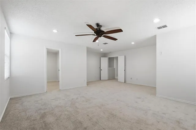 an empty room with chandelier fan and windows