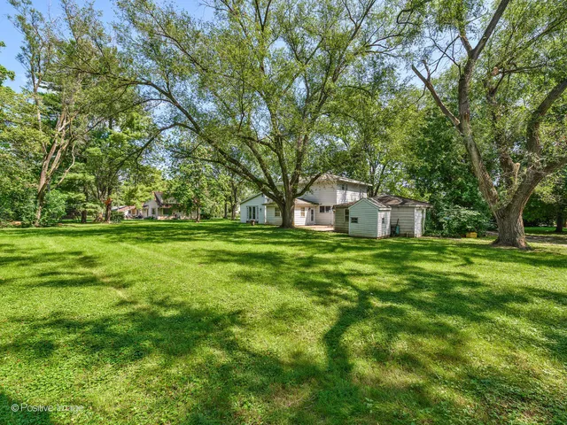a view of a white house in a big yard with large trees