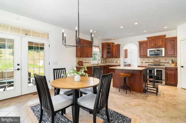 a kitchen with stainless steel appliances kitchen island granite countertop a dining table chairs and a refrigerator