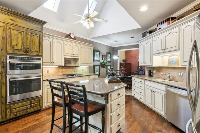a kitchen with stainless steel appliances granite countertop a stove top oven a sink dishwasher and white cabinets with wooden floor