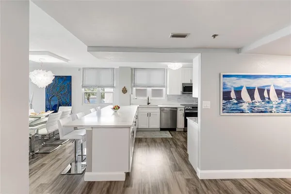 a living room with stainless steel appliances kitchen island granite countertop a refrigerator a sink dishwasher a stove with wooden floor and cabinets