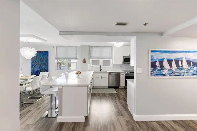 a living room with stainless steel appliances kitchen island granite countertop a refrigerator a sink dishwasher a stove with wooden floor and cabinets