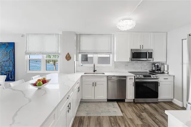 a kitchen with stainless steel appliances granite countertop a stove top oven a sink dishwasher and a refrigerator with wooden floor