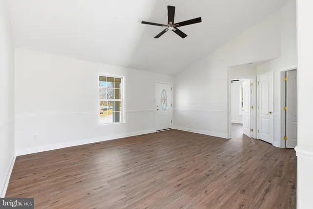 an empty room with wooden floor ceiling fan and windows