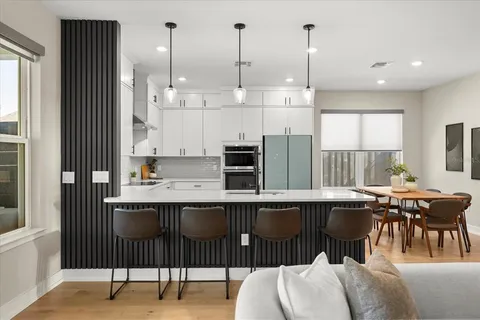 a kitchen with stainless steel appliances granite countertop a stove top oven a sink a dining table and chairs with wooden floor