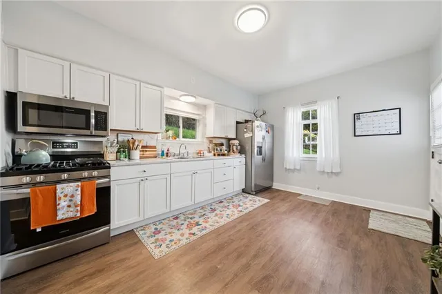 a kitchen with stainless steel appliances a stove a sink dishwasher a microwave oven and a refrigerator with wooden floor