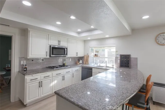 a kitchen with stainless steel appliances granite countertop a stove top oven a sink dishwasher a dining table and chairs with wooden floor