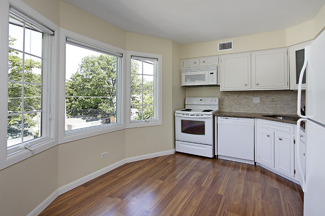 715 Ridge Road, Unit 4E Wilmette, IL 60091 - Photo 4 of 7 a kitchen with granite countertop a stove a sink and white cabinets with wooden floor next to windows