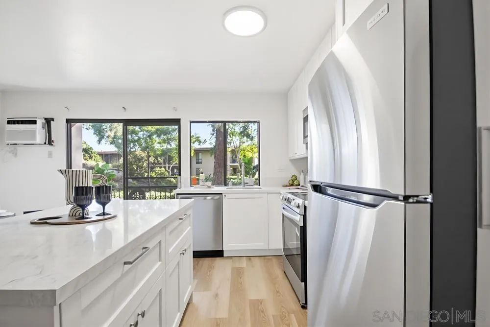 7858 Cowles Mountain Court, Unit D7 San Diego, CA 92119 - Photo 10 of 40 a kitchen with a refrigerator a sink and white cabinets next to a window