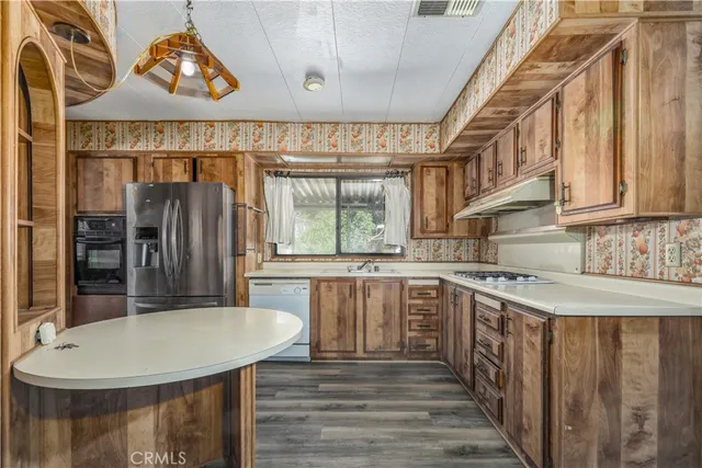a kitchen with stainless steel appliances granite countertop a stove a sink dishwasher and a refrigerator with wooden floor