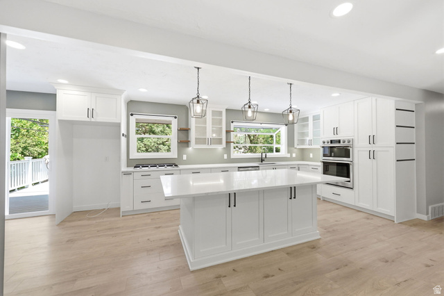 Chef's kitchen featuring white shaker cabinetry, stainless steel built-in appliances, quartz countertops, and a large center island with pendant lighting