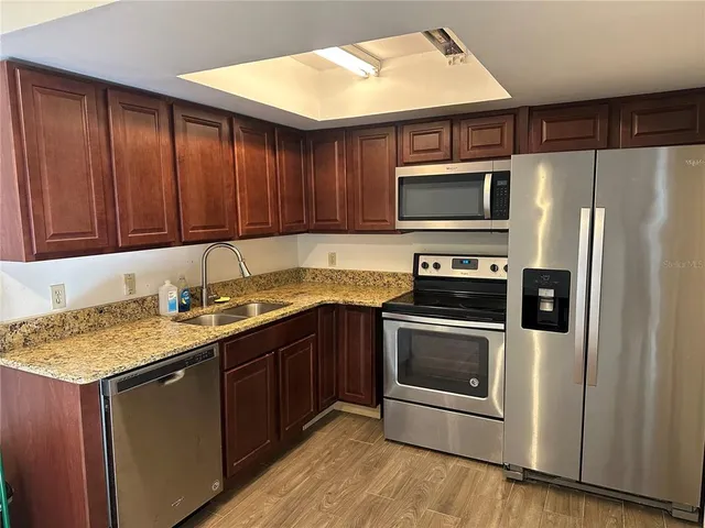 a kitchen with stainless steel appliances granite countertop a refrigerator a stove and a sink with wooden cabinets