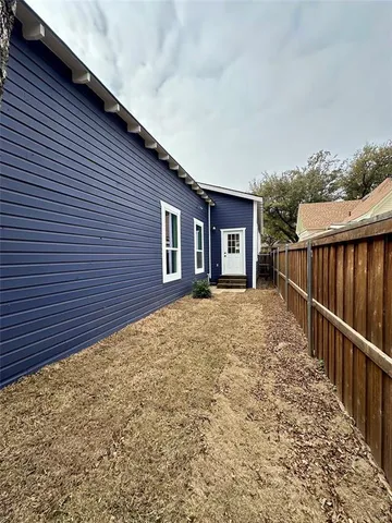 an empty room with wooden floor kitchen view and a window