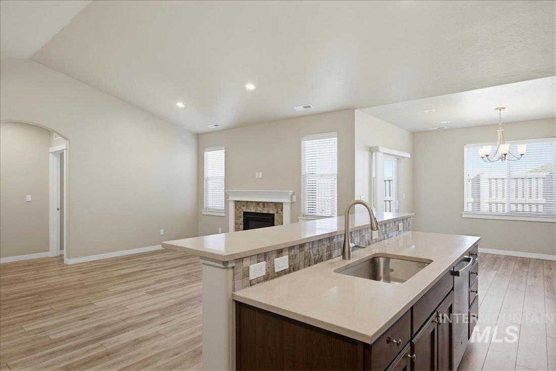 12460 West Azure Street Boise, ID 83713 - Photo 9 of 34 Kitchen island with a stainless steel sink, quartz countertop, dark wood-finish cabinetry, and a stacked stone backsplash