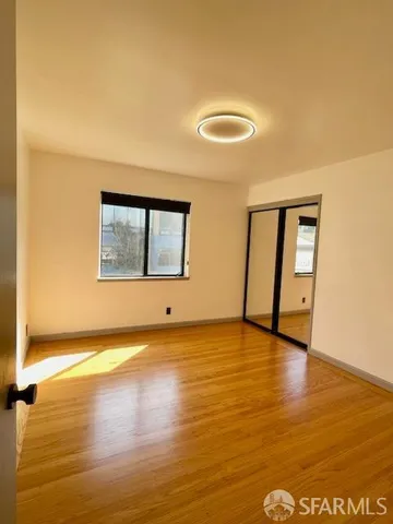 a view of an empty room with wooden floor and a window
