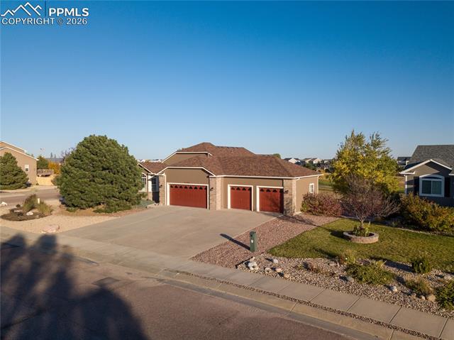 9385 Winged Foot Road Peyton, CO 80831 - Photo 2 of 50 Aerial West/Front View of Ranch-style home with fully manicured front yard, driveway, and a 4-car garage on a corner lot of house with concrete driveway, a 4-car garage with brick and masonite-type siding