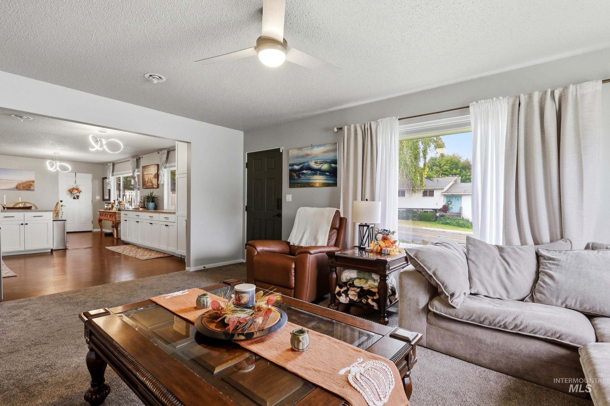 1803 14th Street Lewiston, ID 83501 - Photo 21 of 27 Living area with a ceiling fan light fixture, large window, and an open doorway to an additional room with wood-finish flooring