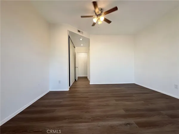 a view of an empty room with wooden floor and a ceiling fan