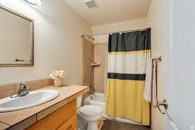 1727 South Sandhill Road Orem, UT 84058 - Photo 23 of 27 Bathroom featuring a built-in vanity with a tiled countertop, undermount sink, and wood-finish cabinetry