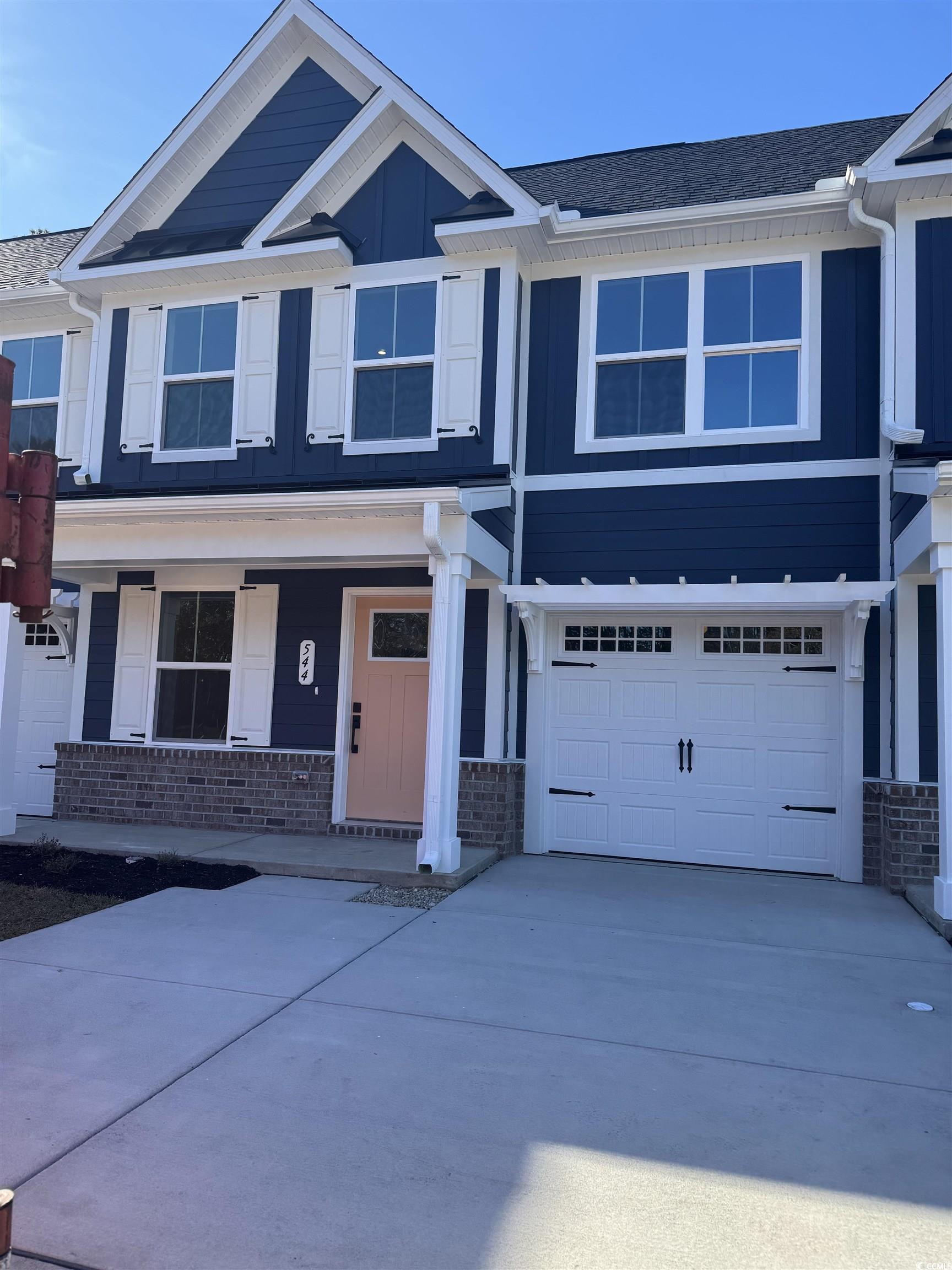 View of front of home with a porch, a garage, driveway, brick siding, and roof with shingles